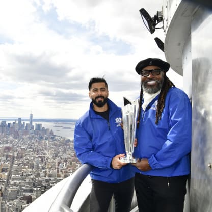 Ali Khan and Chris Gayle with the ICC Men's T20WC Trophy and the view of downtown Manhattan