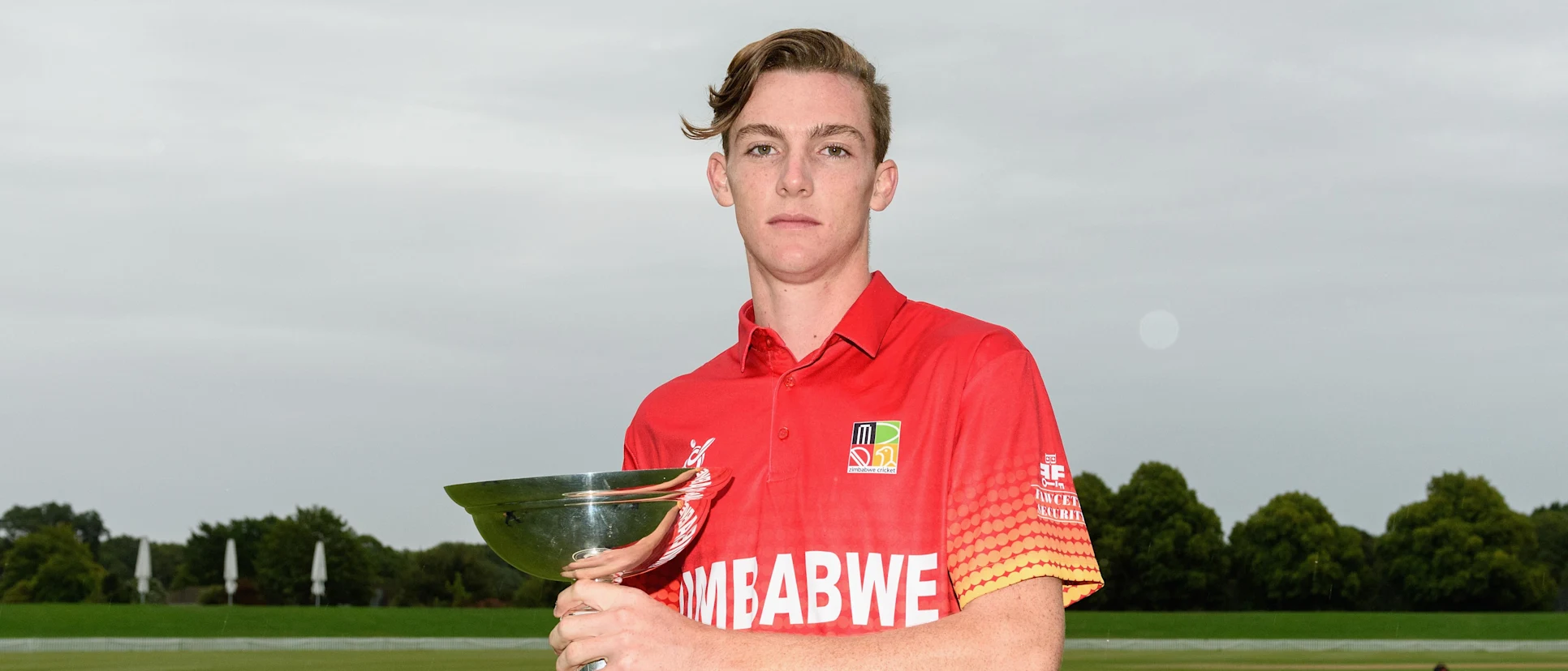 Logo of Zimbabwe U19 captain Liam Roche poses with the ICC Under 19 Cricket World Cup trophy.