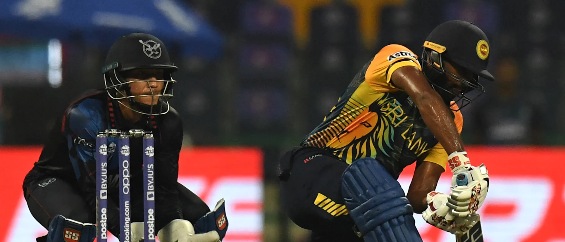 Logo of Bhanuka Rajapaksa (R) plays a shot as Namibia's wicketkeeper Zane Green watches during the ICC mens Twenty20 World Cup cricket match between Namibia and Sri Lanka at the Sheikh Zayed Stadium in Abu Dhabi on October 18, 2021.