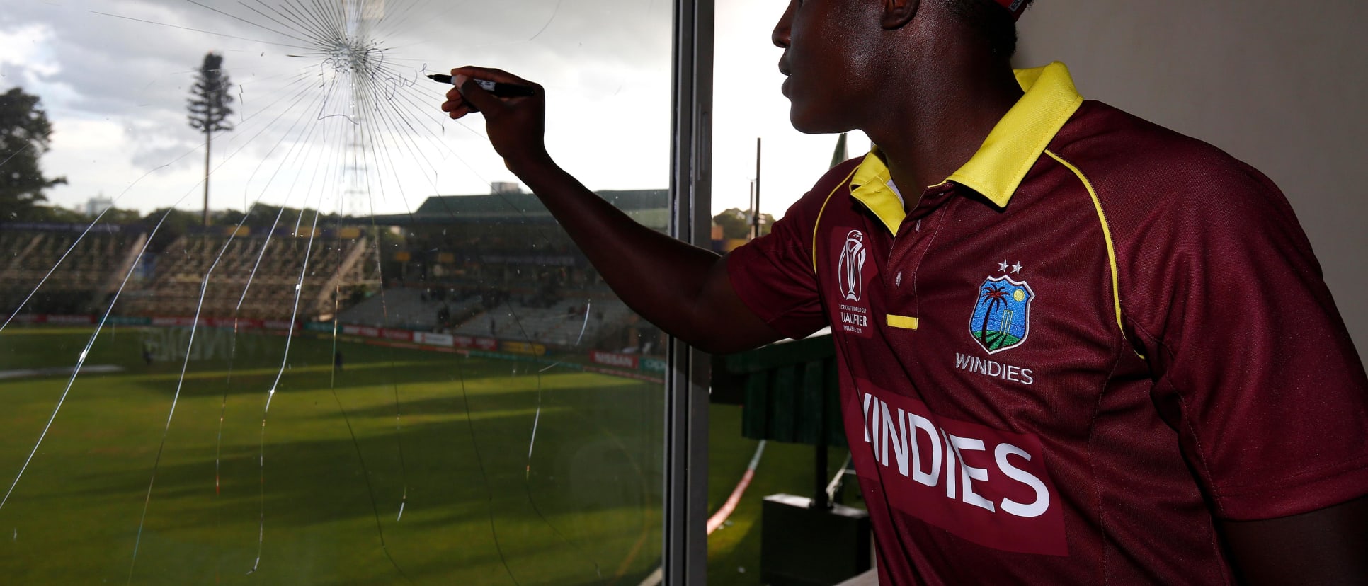 Rovman Powell of The Windies signs a window he broke in the press room whilst batting during The ICC Cricket World Cup Qualifier between The Windies and Ireland at The Harare Sports Club on March 10, 2018 in Harare, Zimbabwe (©ICC).